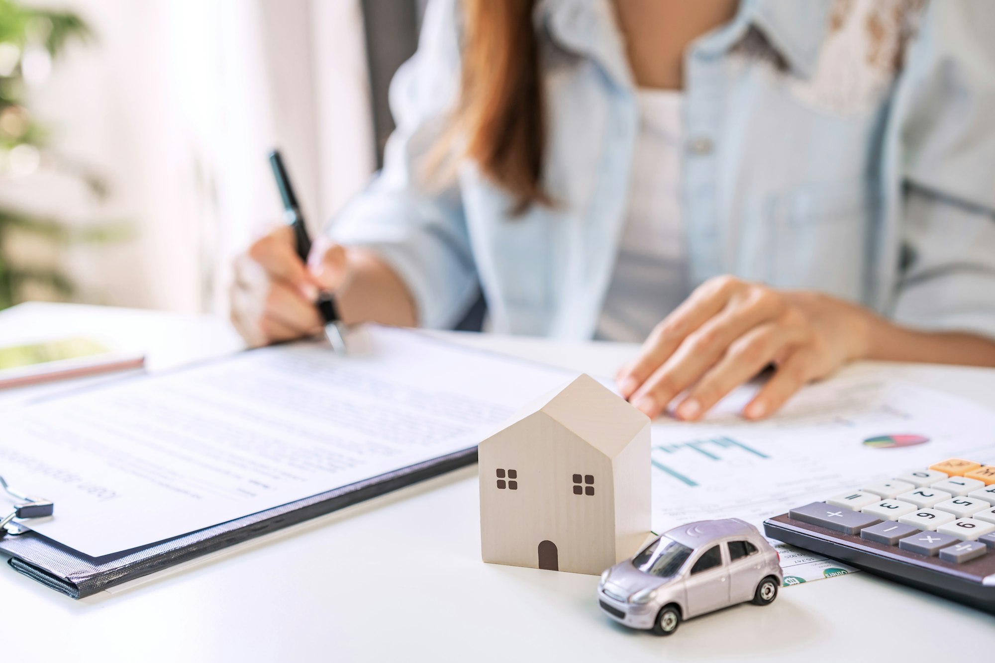 Young woman is signing a loan agreement to buy a house and a car at real estate agent office